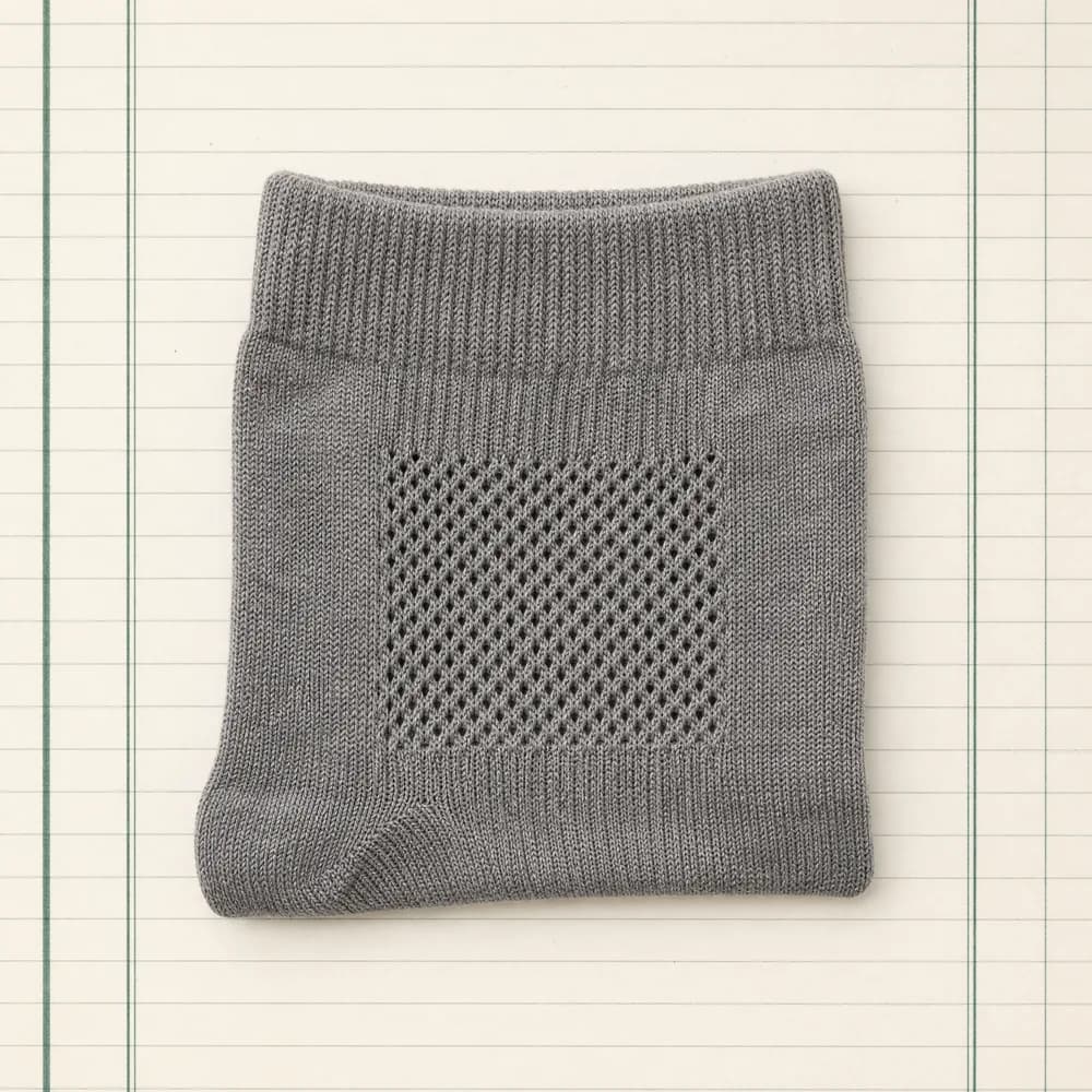 A sock with a knitted mesh ventilation zone, folded flat on ruled paper.